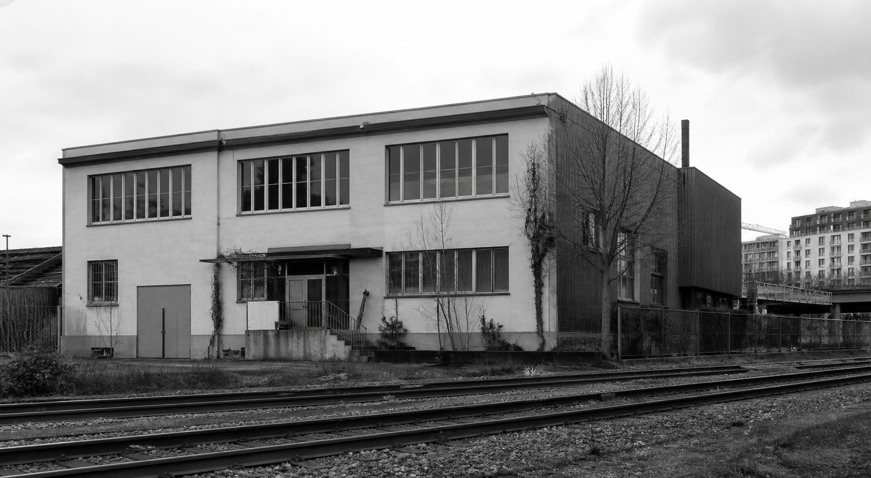 Schwarzweisse Ansicht eines schlichten Ateliergebäudes an Bahngeleisen